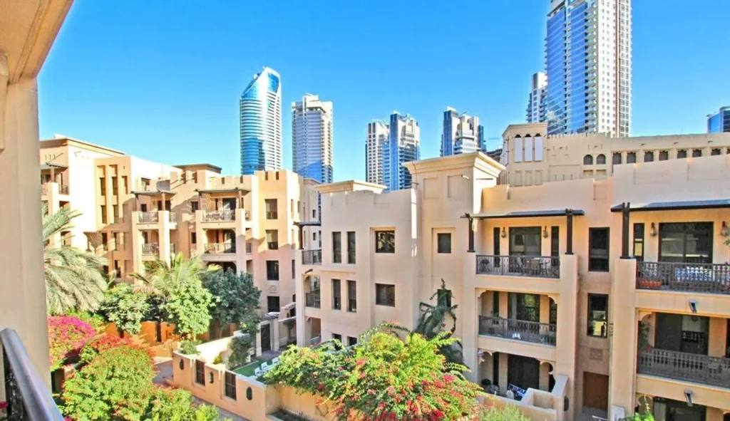 Old Town Dubai sandstone apartments with bougainvillea gardens and modern towers behind — buy property in Dubai from Australia
